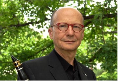 James Campbell wearing a suit and red glasses, holding a clarinet.